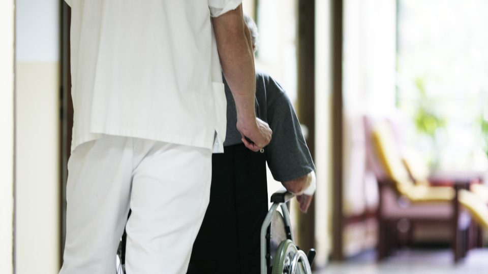 Pfleger schiebt Person im Rollstuhl